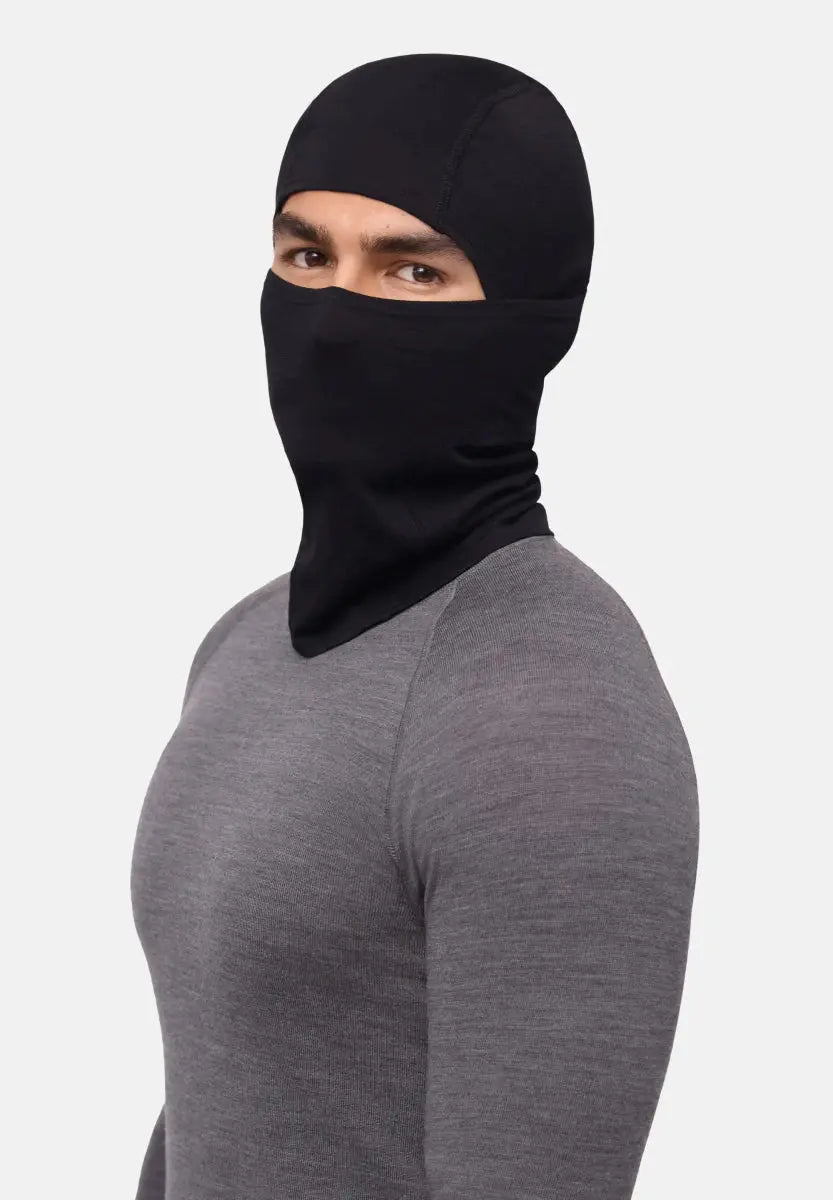 Person wearing a black balaclava and gray shirt, eyes visible, against a white background.