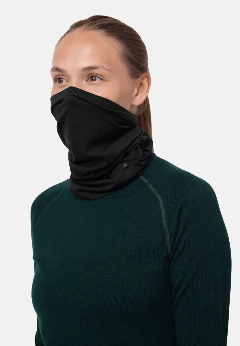 Person wearing a black merino neck gaiter covering lower face, with a dark green shirt.