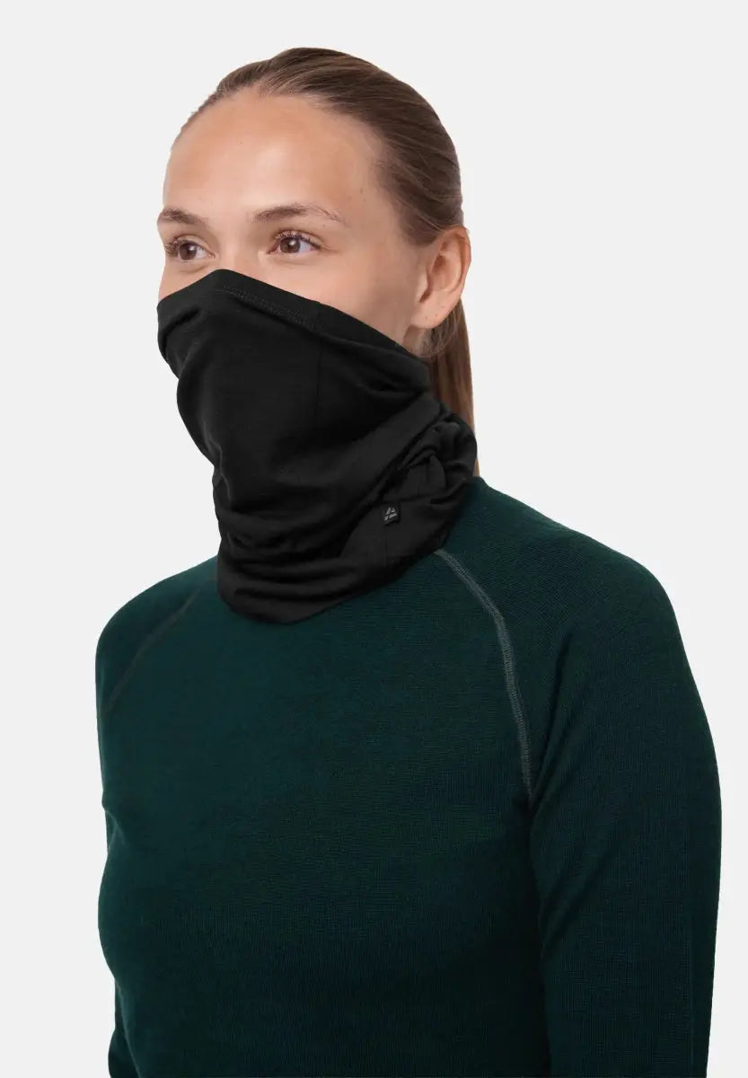 Person wearing a black merino neck gaiter covering lower face, with a dark green shirt.