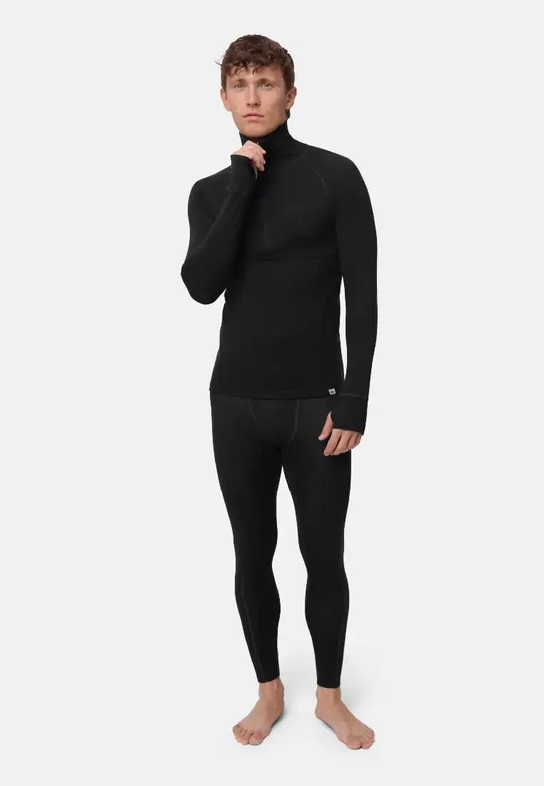 Man in black merino wool base layer half-zip shirt and leggings, standing barefoot on a light background.