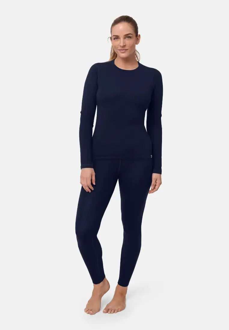 Woman in dark blue merino wool base layer set, standing barefoot on a light background.