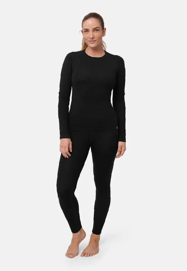 Woman in black merino wool base layer set, with long-sleeve top and leggings, standing barefoot.