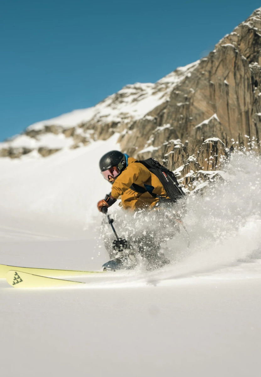 Skier in action on snowy slope, wearing helmet and goggles, creating snow spray.