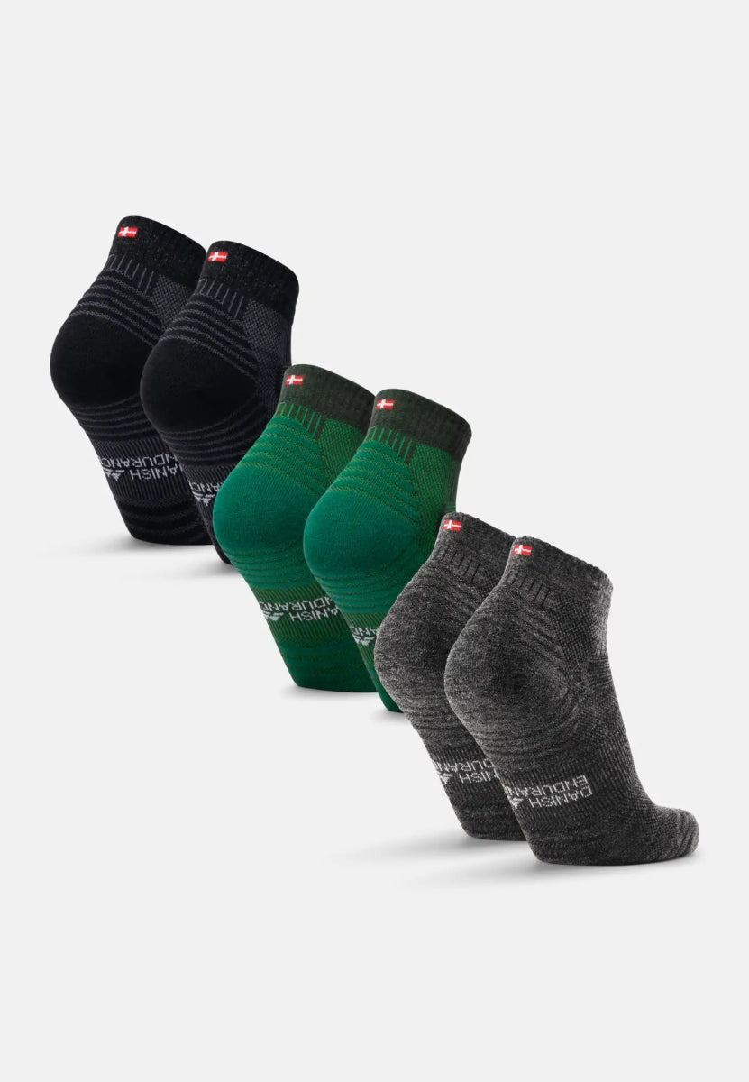 Three pairs of low-cut merino wool hiking socks in black, green, and gray with a flag detail.