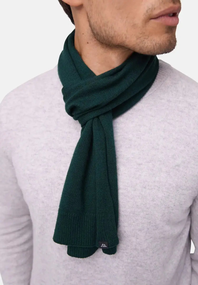 Dark green Merino wool scarf on person wearing light gray sweater, small tag on scarf visible.