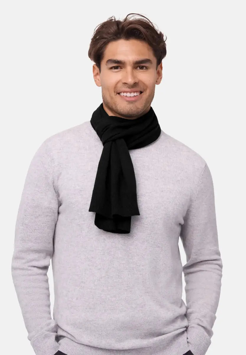 Person wearing black merino wool scarf over a light grey sweater, smiling warmly.