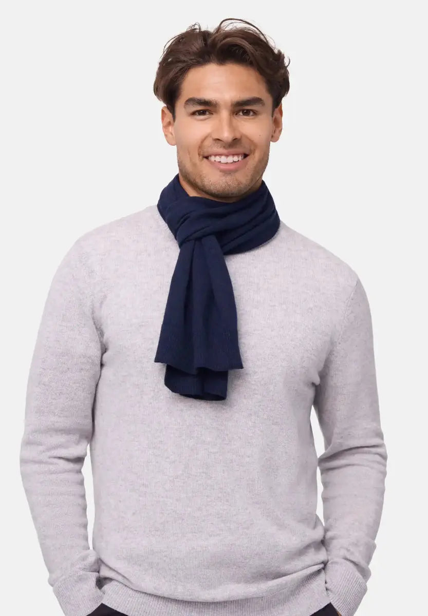 Navy blue merino wool scarf worn by a person over a light gray sweater, smiling with hands in pockets.