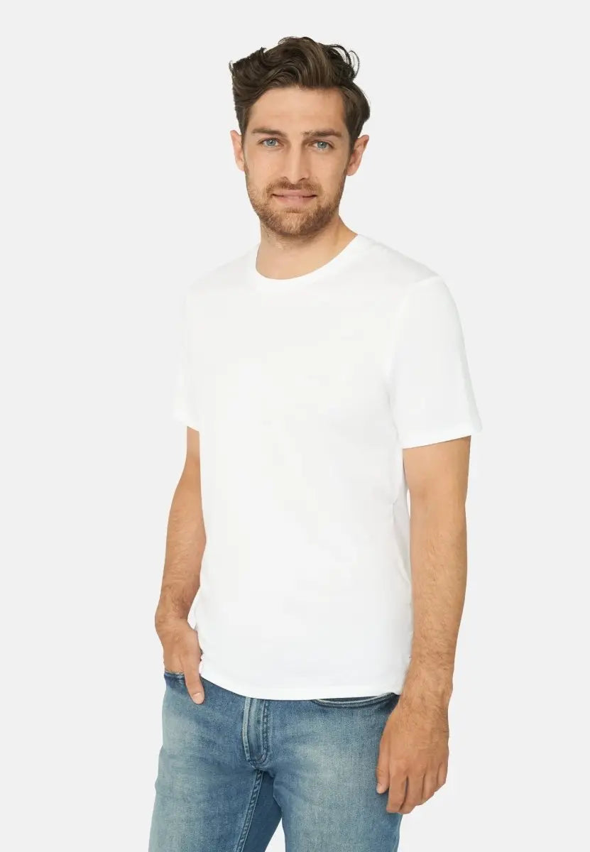 Man wearing a white crew neck t-shirt and blue jeans, standing against a plain background.