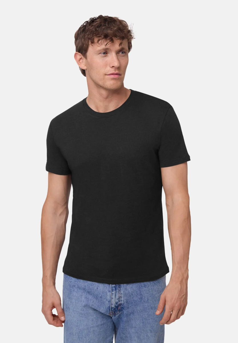 Man wearing black crew neck t-shirt and blue jeans, standing against a plain white background.