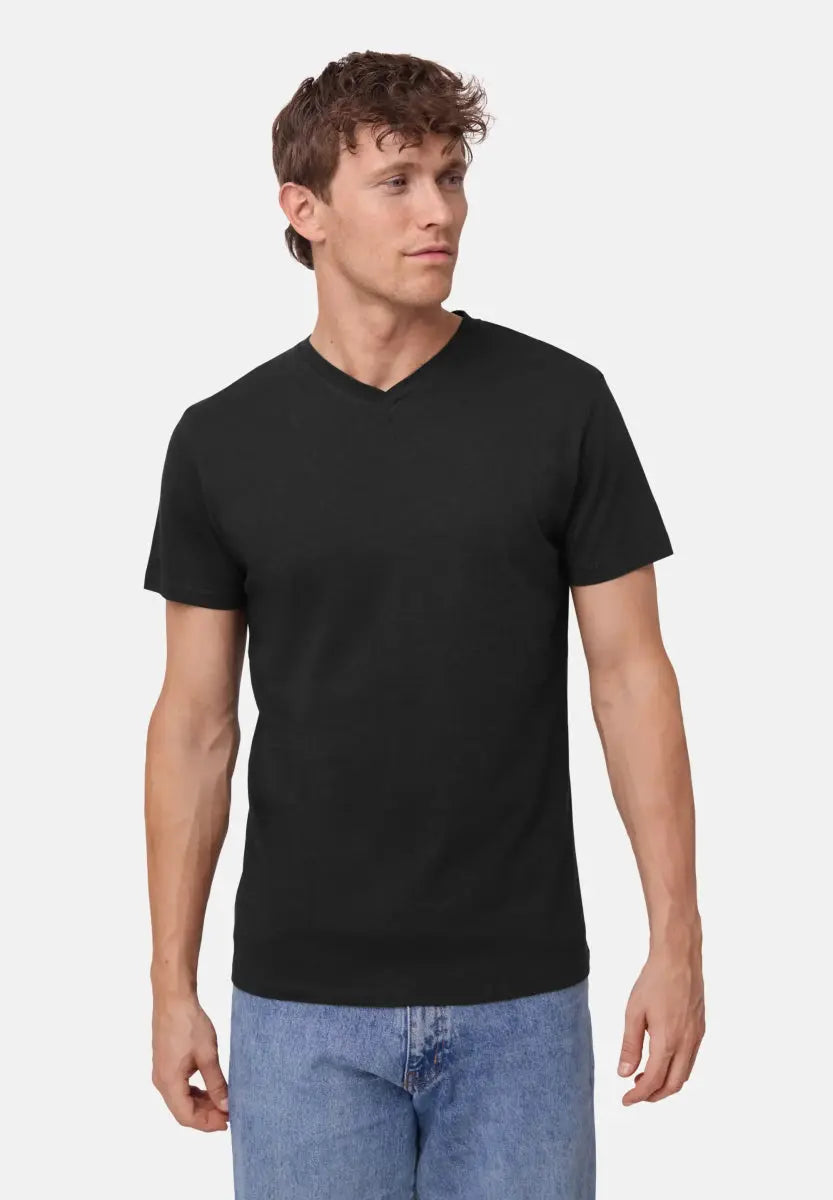 Man wearing a black V-neck T-shirt and blue jeans, looking to the side against a plain background.