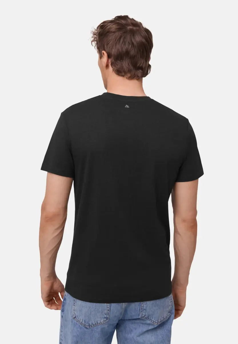 Back view of a man in a black V-neck T-shirt and blue jeans against a plain background.