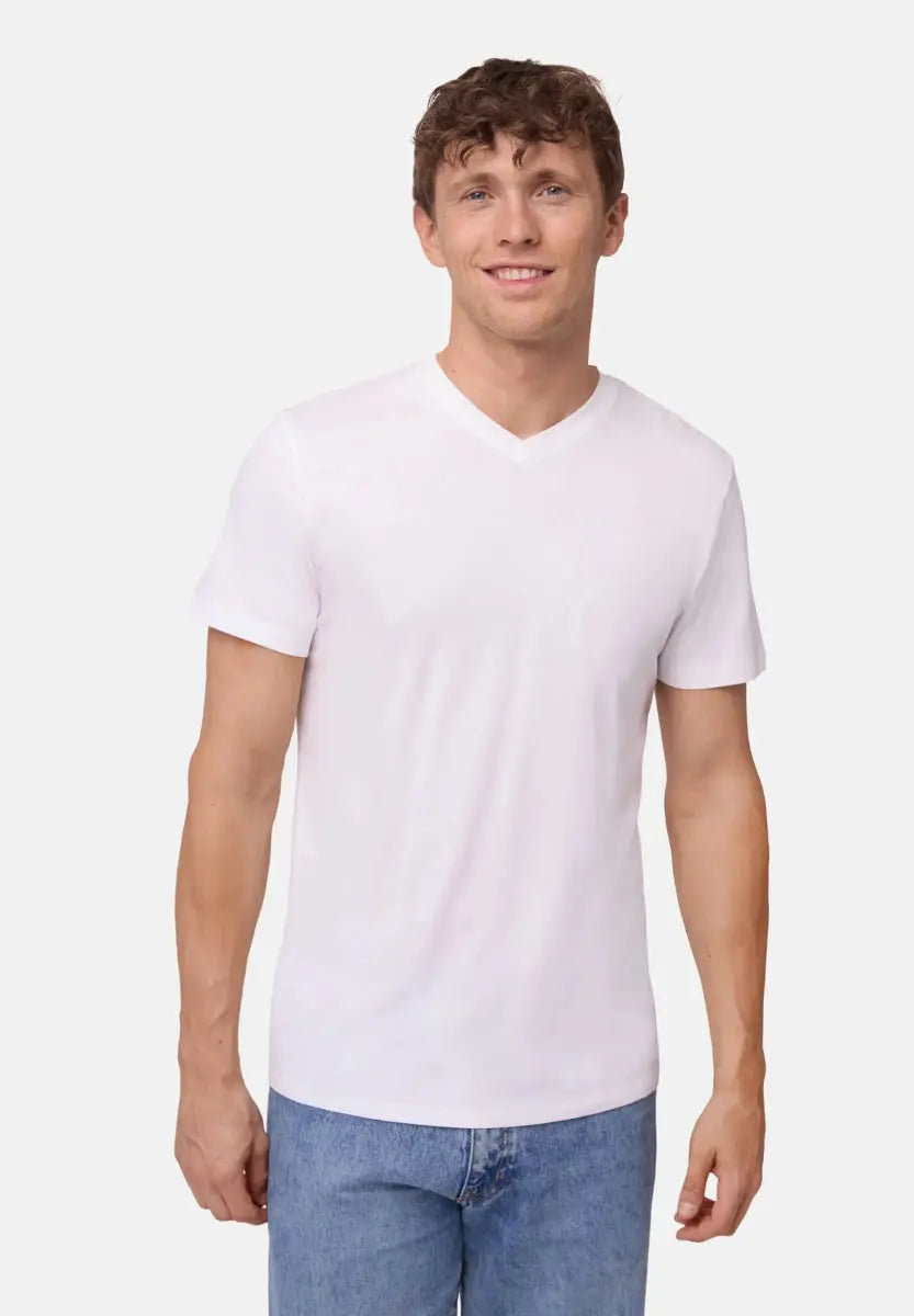 Man in white V-neck T-shirt and blue jeans, standing against a plain background, smiling.