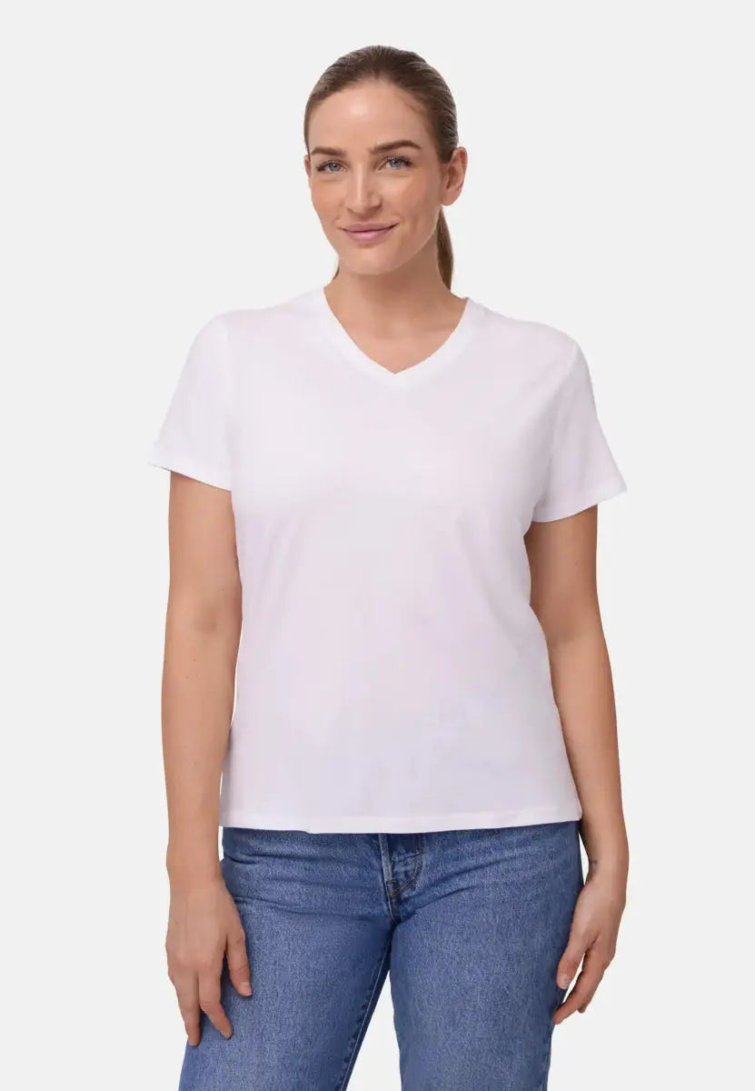 Woman in a white V-neck T-shirt and blue jeans, standing and smiling against a plain background.
