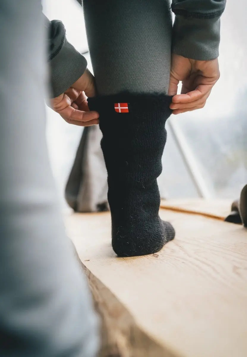 Person adjusting black sock with red and white flag emblem, on a wooden floor.