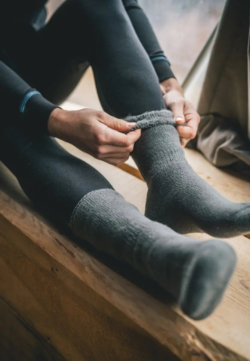 Person wearing gray non-slip heat socks, sitting on a wooden bench, adjusting one sock.