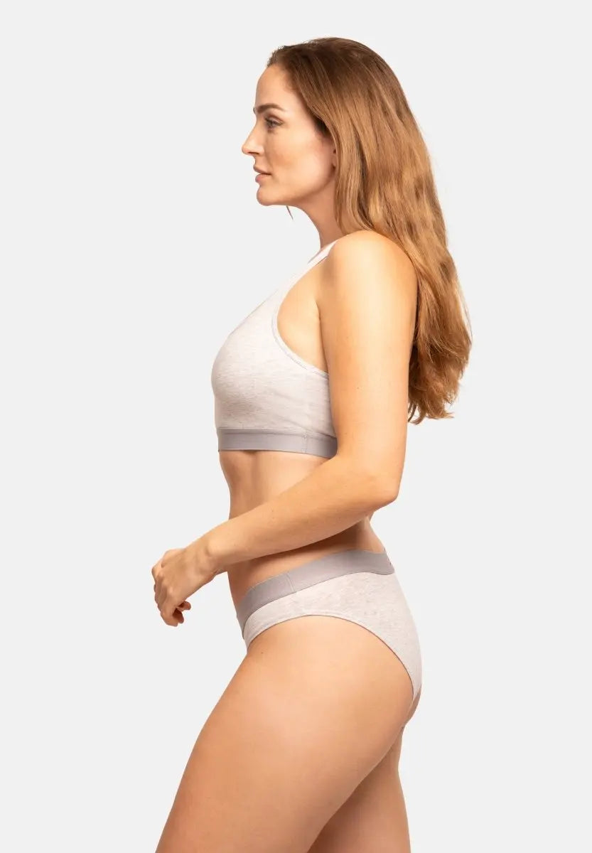 Woman in profile wearing light grey organic cotton bikini panties and matching bra against a white background.