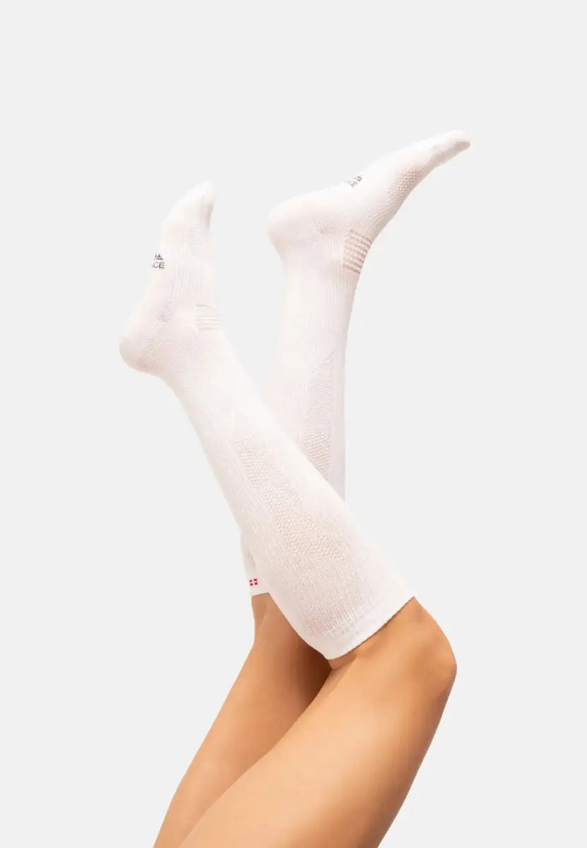 Two legs wearing white knee-high organic cotton compression socks, raised against a plain background.