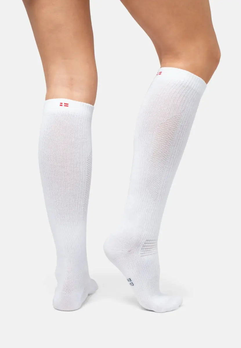 Legs wearing knee-high white compression socks with red logo at the top on a neutral background.