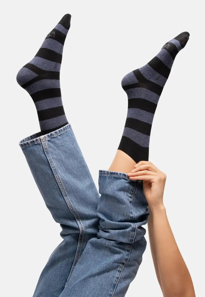 Feet in black and gray striped socks, legs in blue jeans raised playfully against a white background.