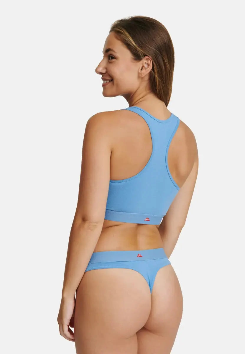 Woman in light blue thong and matching racerback bra, viewed from the back, smiling.