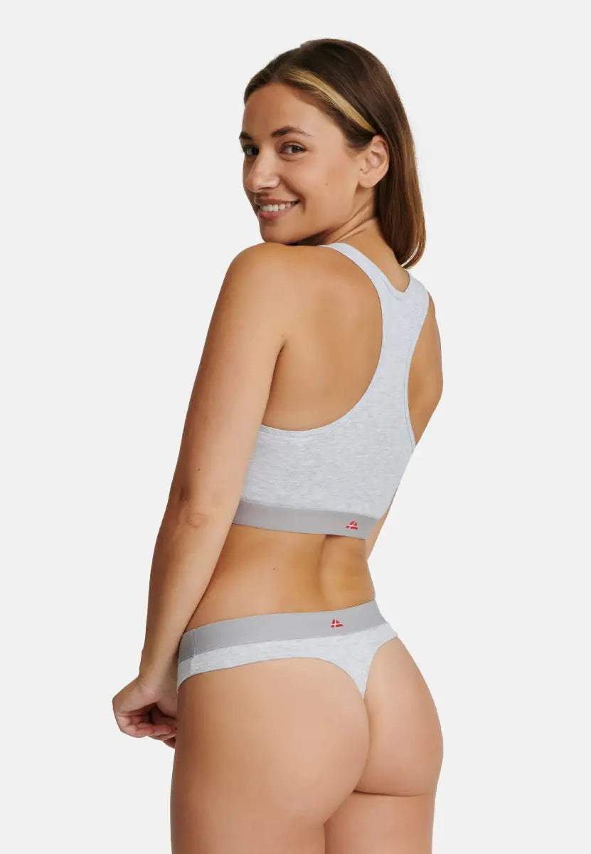 Woman in light grey sports bra and thong, viewed from the back, smiling over her shoulder.