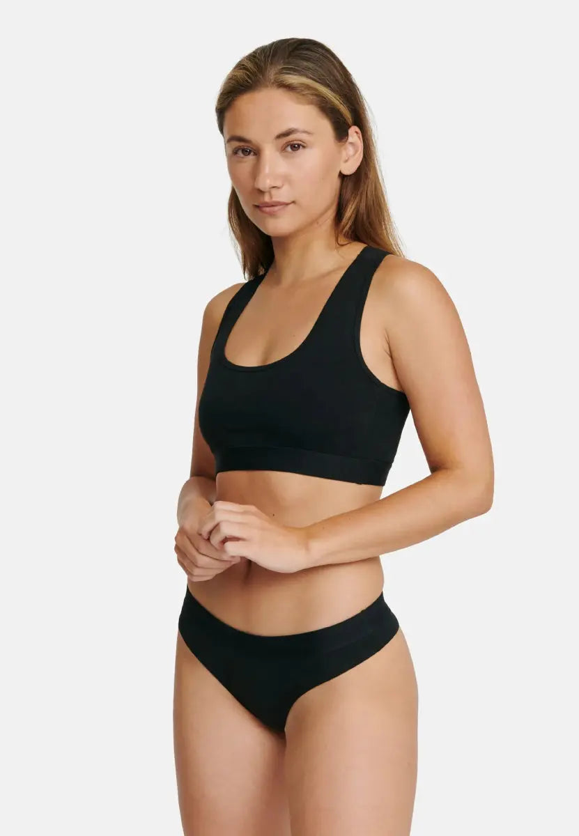 Woman in black organic cotton thong and crop top against white background.
