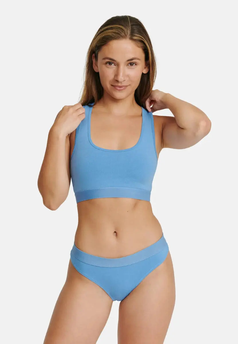 Woman in blue organic cotton thong and matching crop top against a plain background.