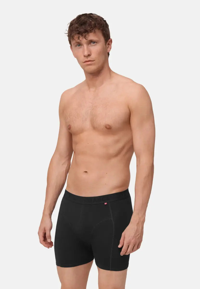 Man wearing black organic cotton trunks, showcasing fit and style against a plain background.