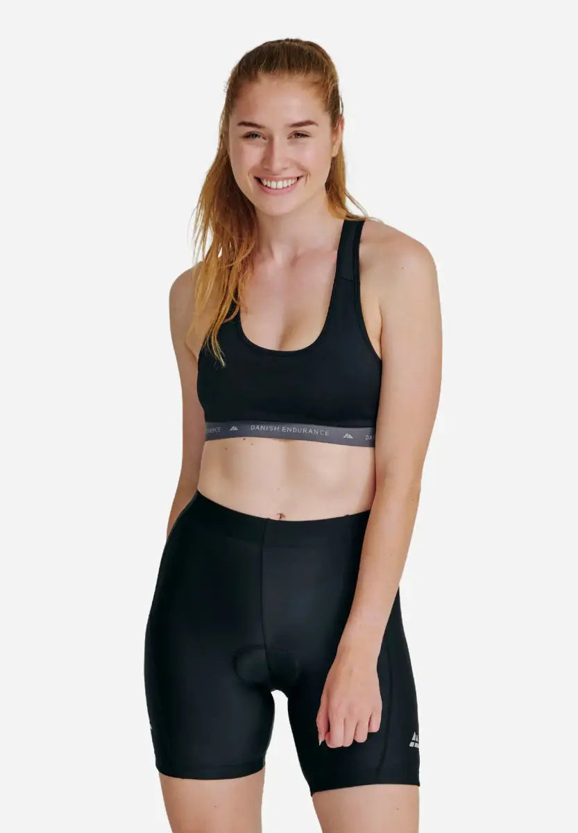 Woman in black padded bike shorts and sports bra, smiling against a plain white background.