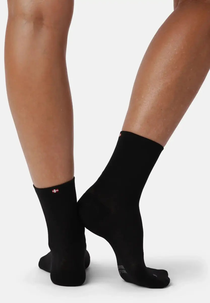 Two legs wearing black plantar fasciitis socks with a small emblem on a plain background.