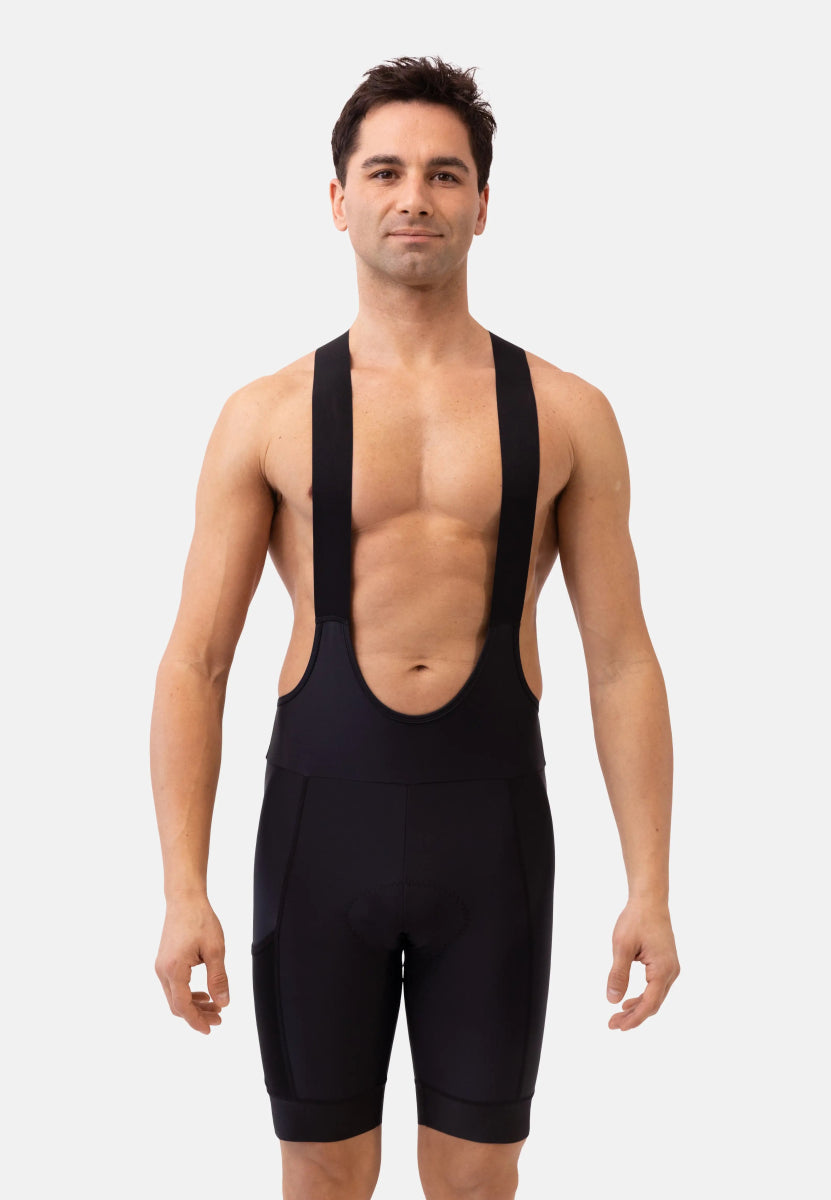 Man wearing black bib shorts with shoulder straps, standing against a plain white background.