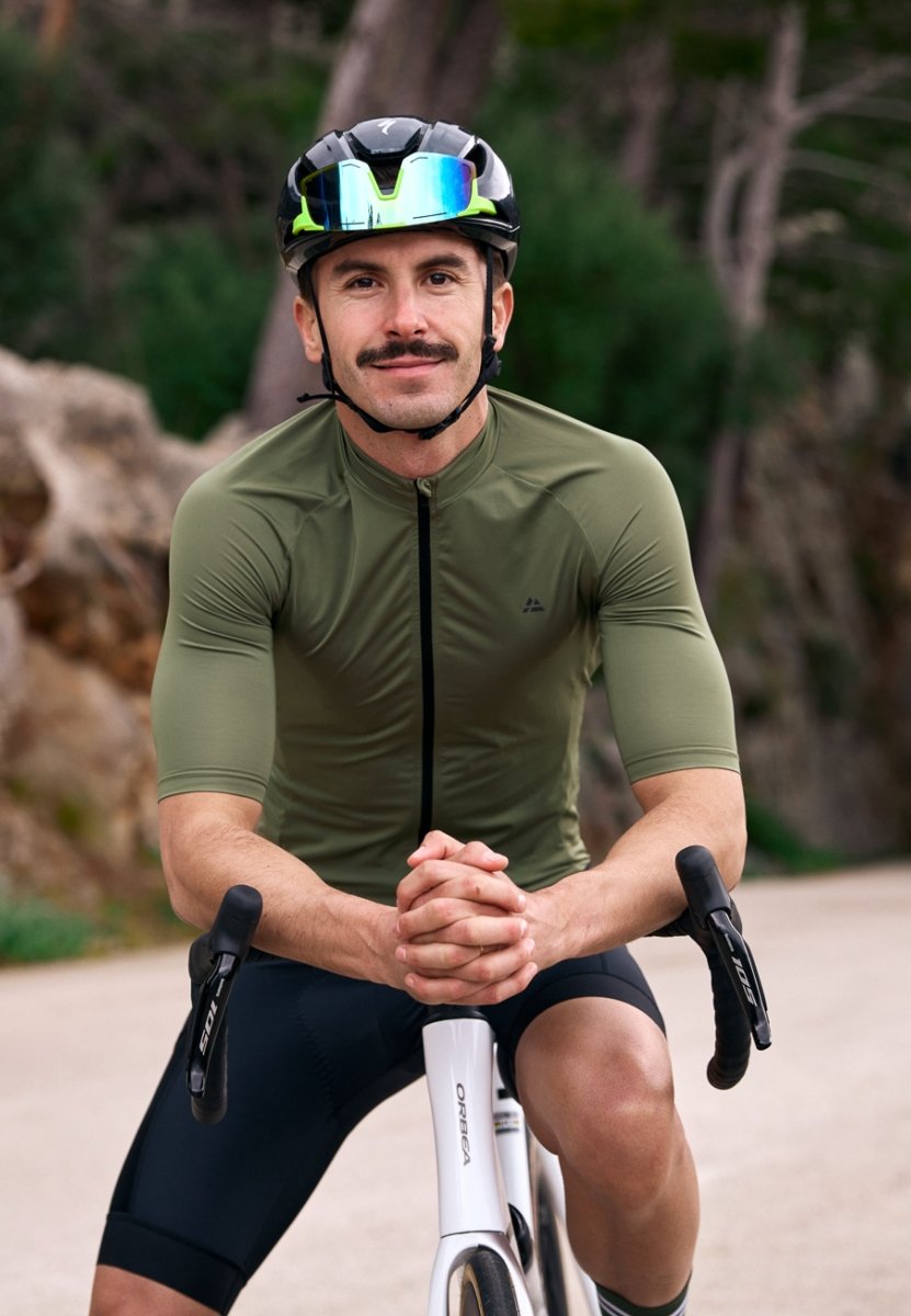 Man in green cycling jersey and helmet on a white bike, outdoors.