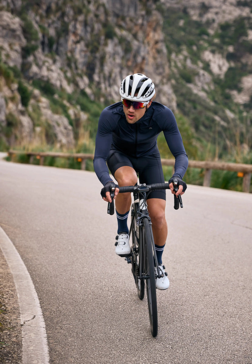 Cyclist wearing pro cycling shorts, helmet, and sunglasses, riding uphill on a winding road.