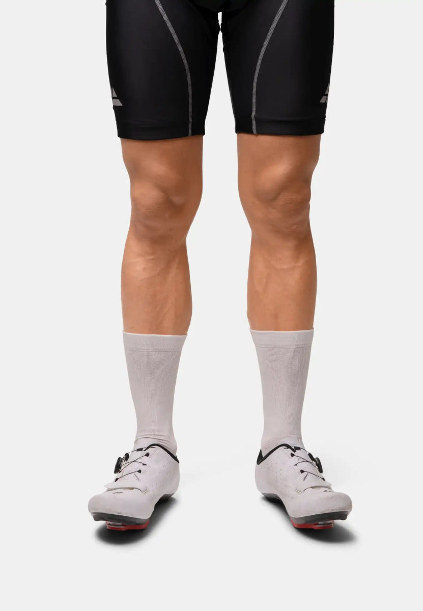 Person wearing black cycling shorts, white socks, and cycling shoes standing on a plain background.