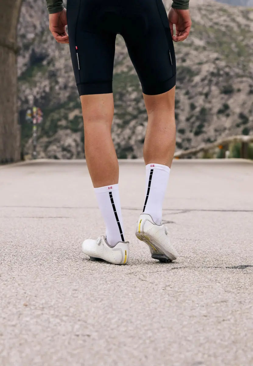 Cyclist wearing white socks with black stripes and white shoes on a mountain road.