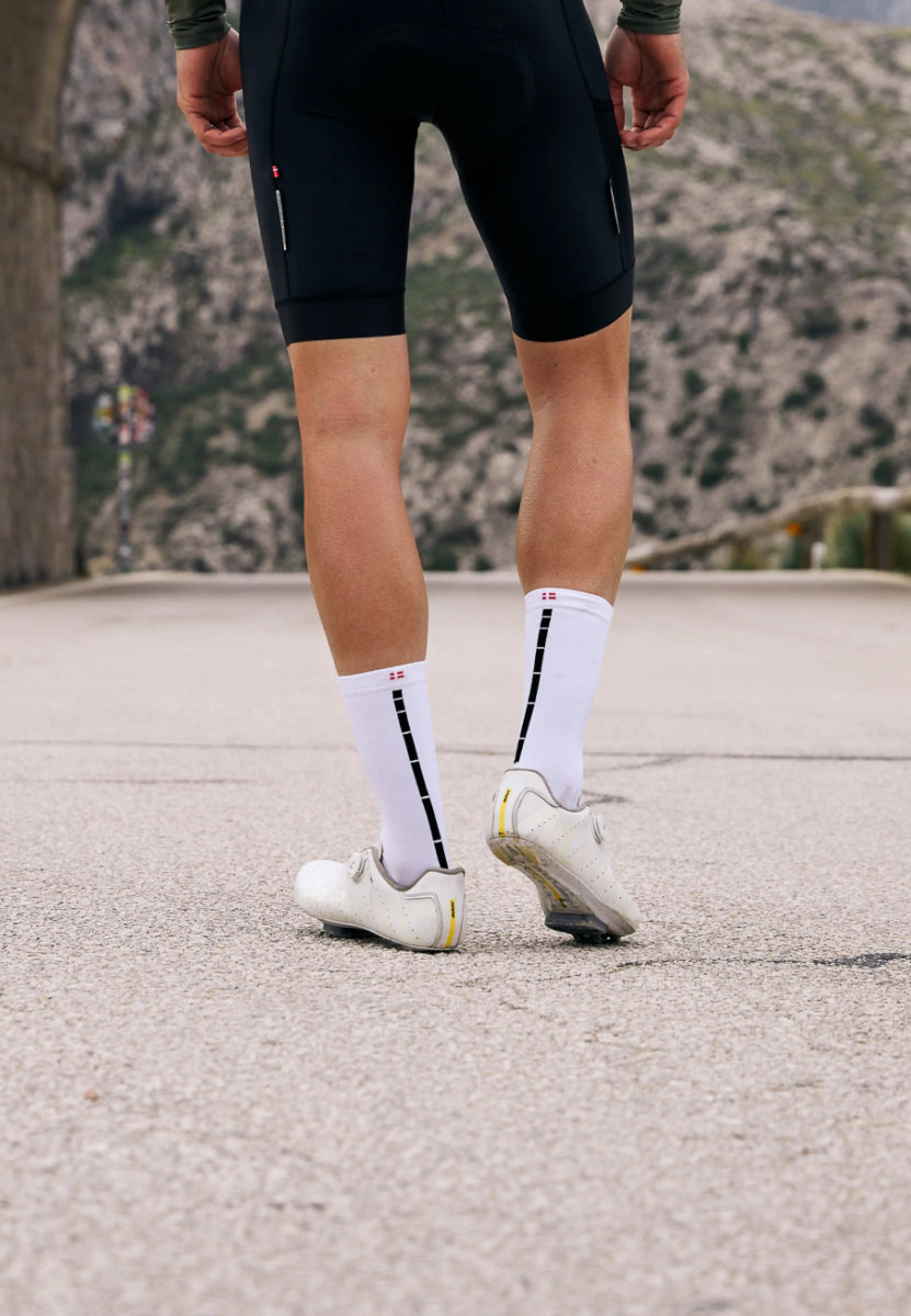 Person in cycling gear, white socks with black stripes, white shoes, mountain road backdrop.