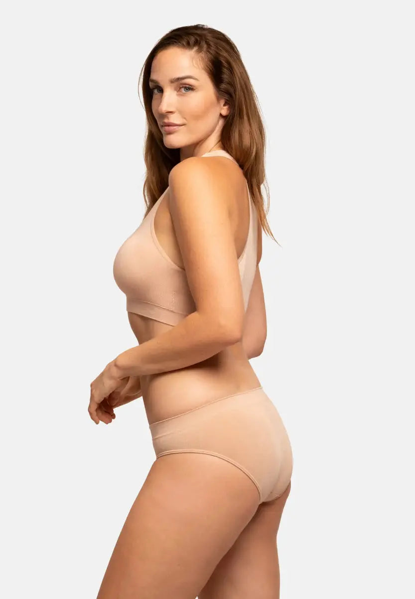 Woman in nude seamless bamboo bikini, side profile against white background.