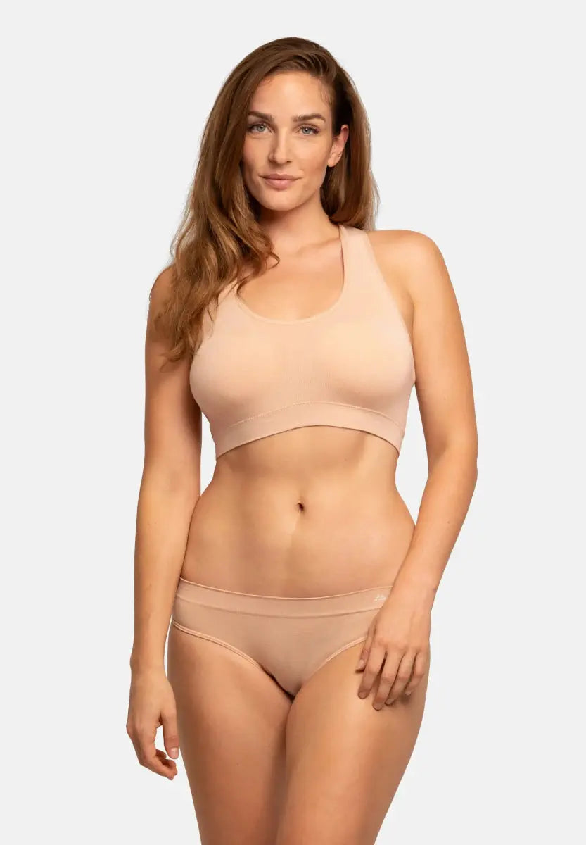 Woman in neutral seamless bamboo bikini, standing confidently against a plain background.