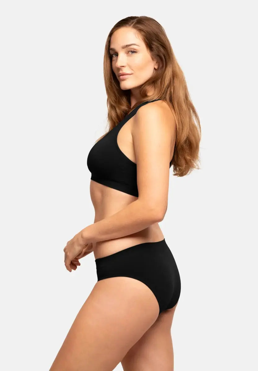 Woman in a black seamless bamboo bikini, side view, long hair, neutral expression.
