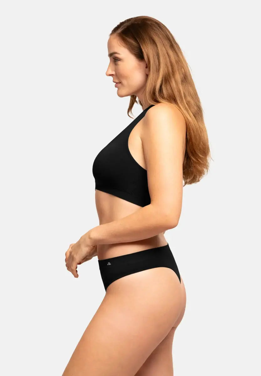 Woman in black seamless bamboo thong and bra, side view, with long hair and neutral background.