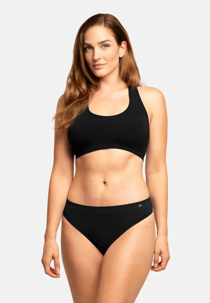 Woman in black seamless bamboo thong and matching sports bra, standing against a plain background.