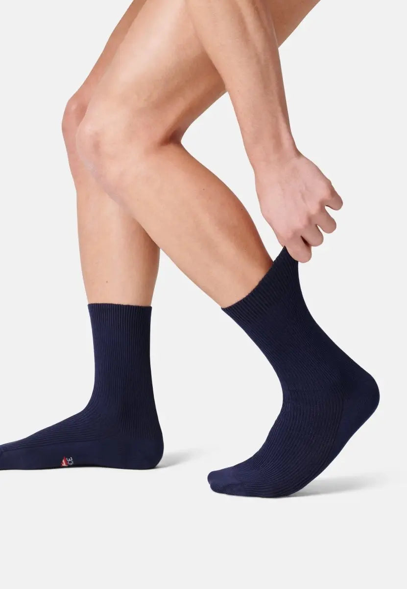 Person putting on navy blue ribbed crew socks, showing soft texture and snug fit.