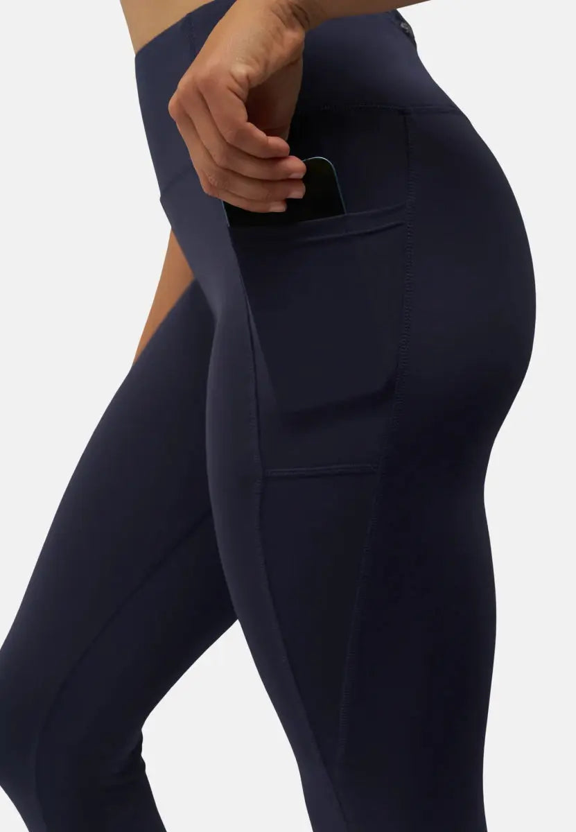 Dark blue leggings with side pocket, hand placing a phone in the pocket, emphasizing functionality.