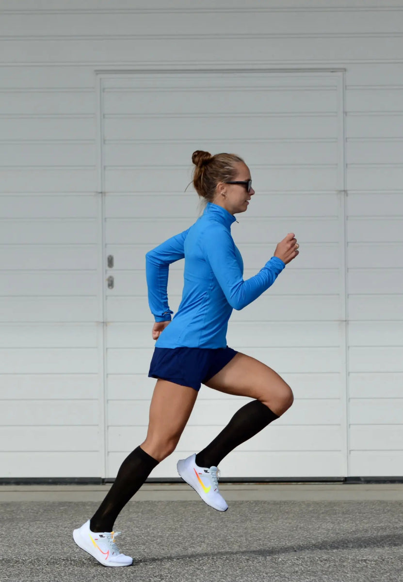 Person running in black compression socks, blue top, navy shorts, and white sneakers.