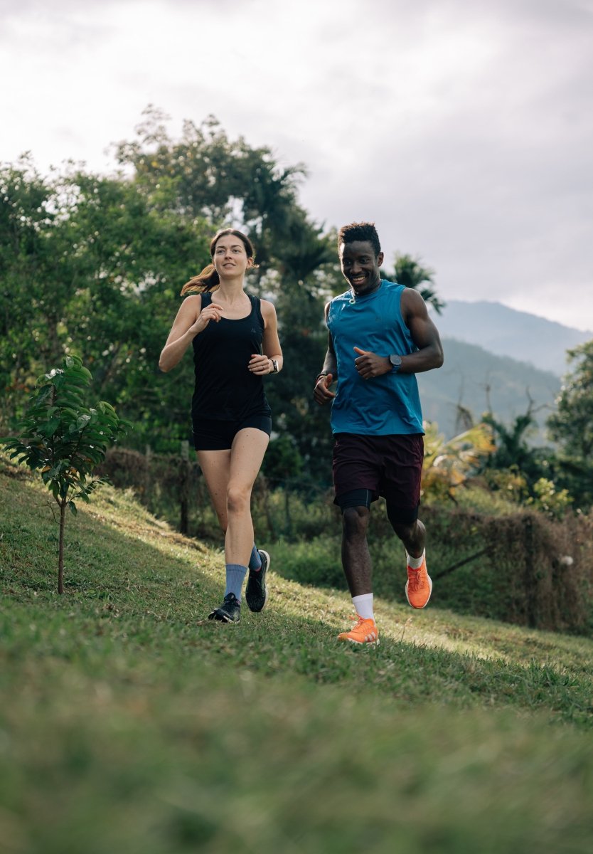 Woman in black tank top and man jogging on a grassy path with trees and hills in the background.