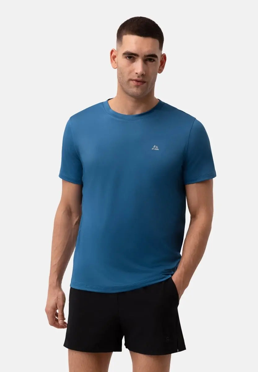 Man in blue performance T-shirt and black shorts, standing with one hand in pocket.