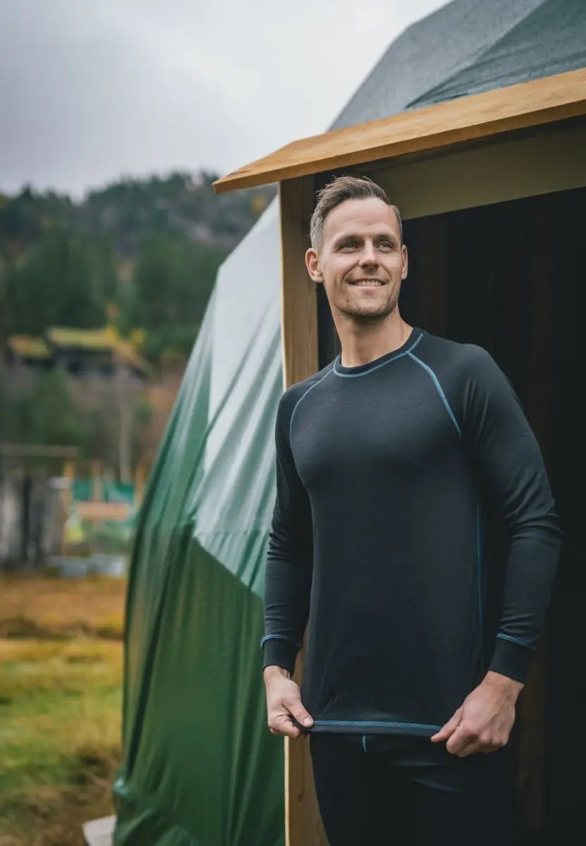 Person wearing black thermal underwear outside a wooden structure with trees in the background.