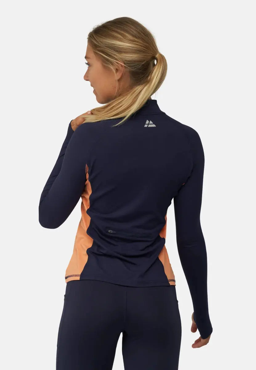 Woman in navy athletic shirt with peach sides, logo on back, zippered pocket, ponytail hairstyle.