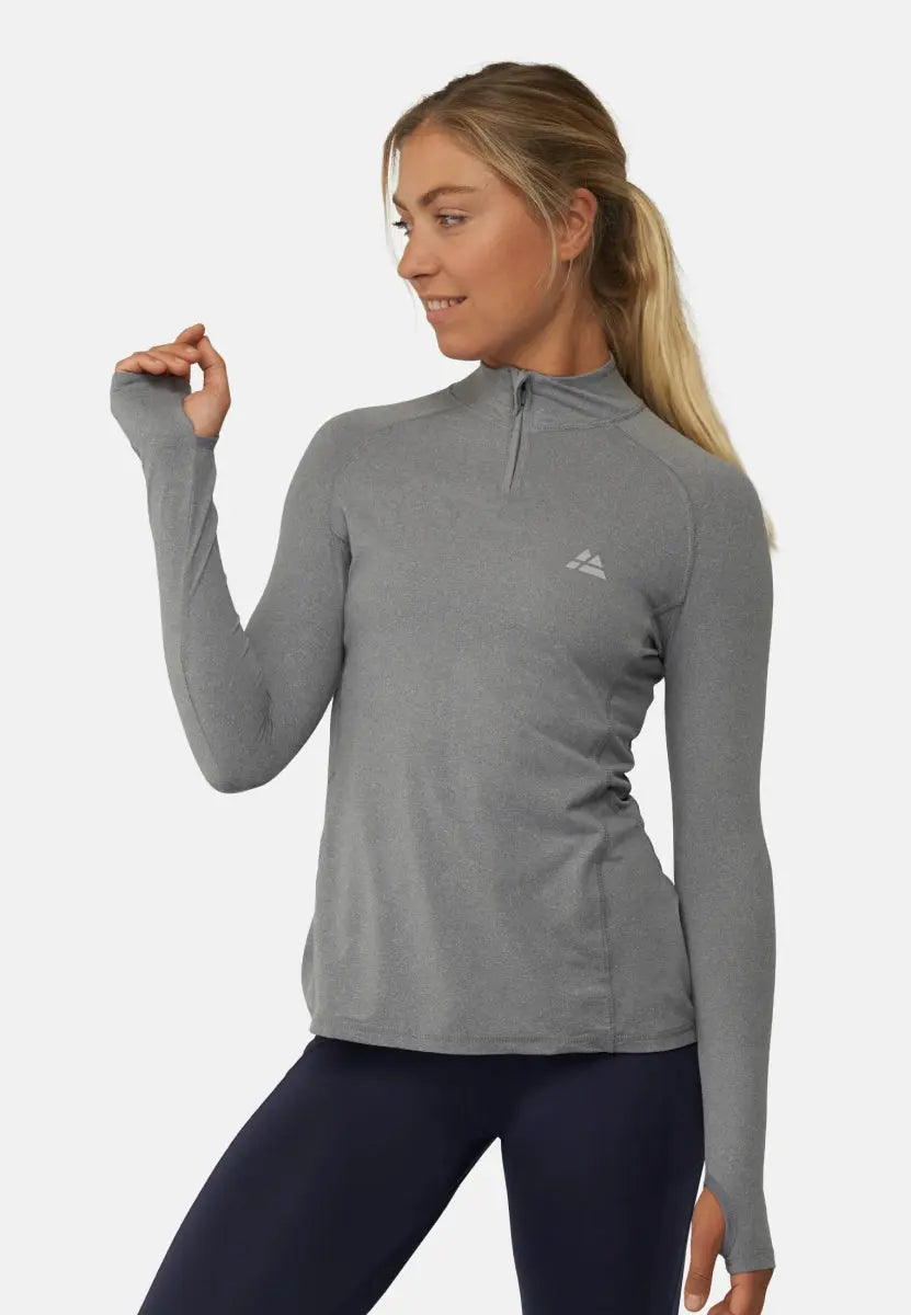 Woman in gray long sleeve athletic shirt with logo, ponytail, and relaxed pose.
