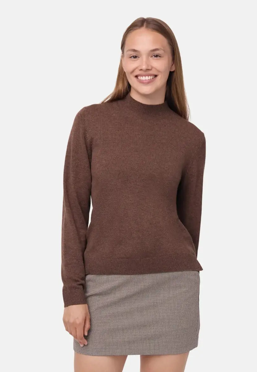 Woman in a brown merino cashmere sweater and checkered skirt, smiling against a plain background.